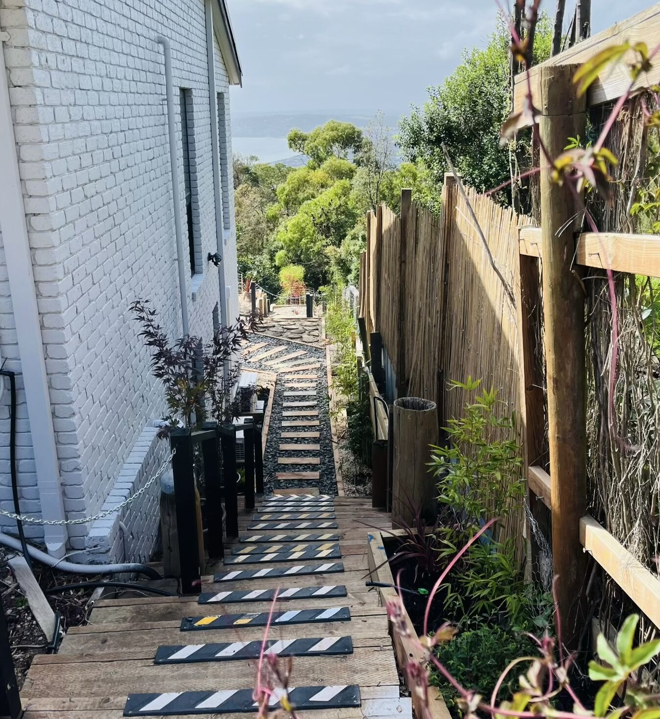 A narrow pathway leading to a wooden deck, flanked by a white brick wall and a wooden fence.
