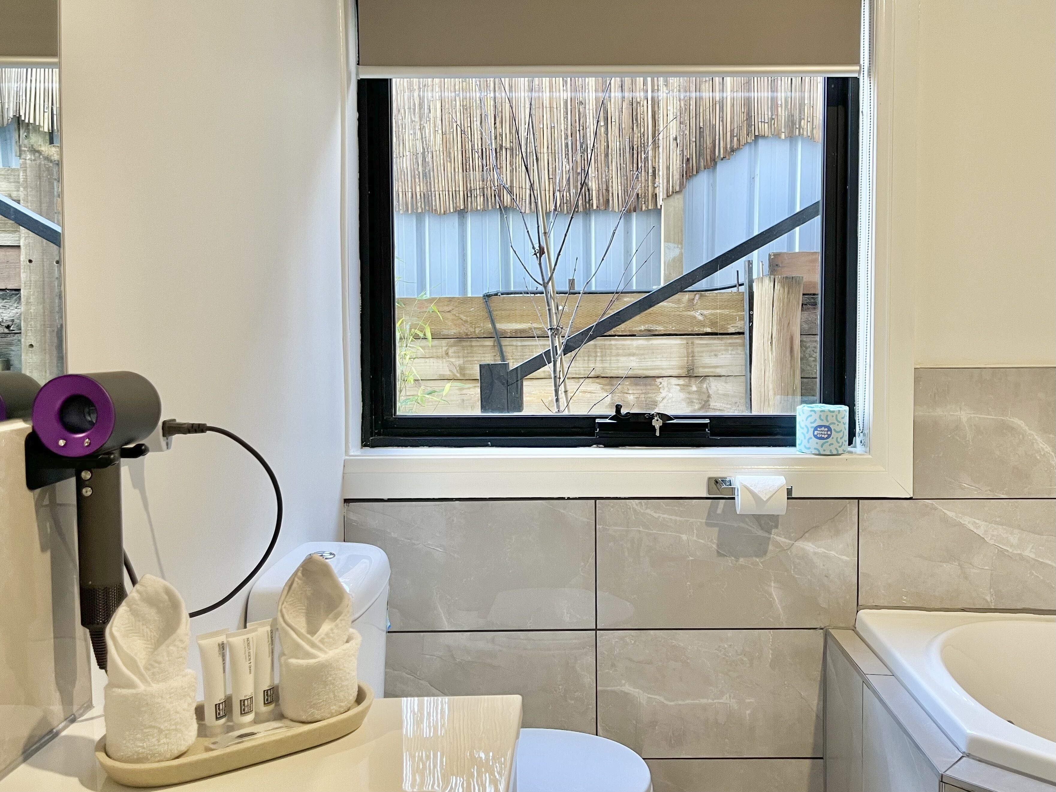 Une salle de bain avec une fenêtre, un sèche-cheveux, une serviette et des articles de toilette.