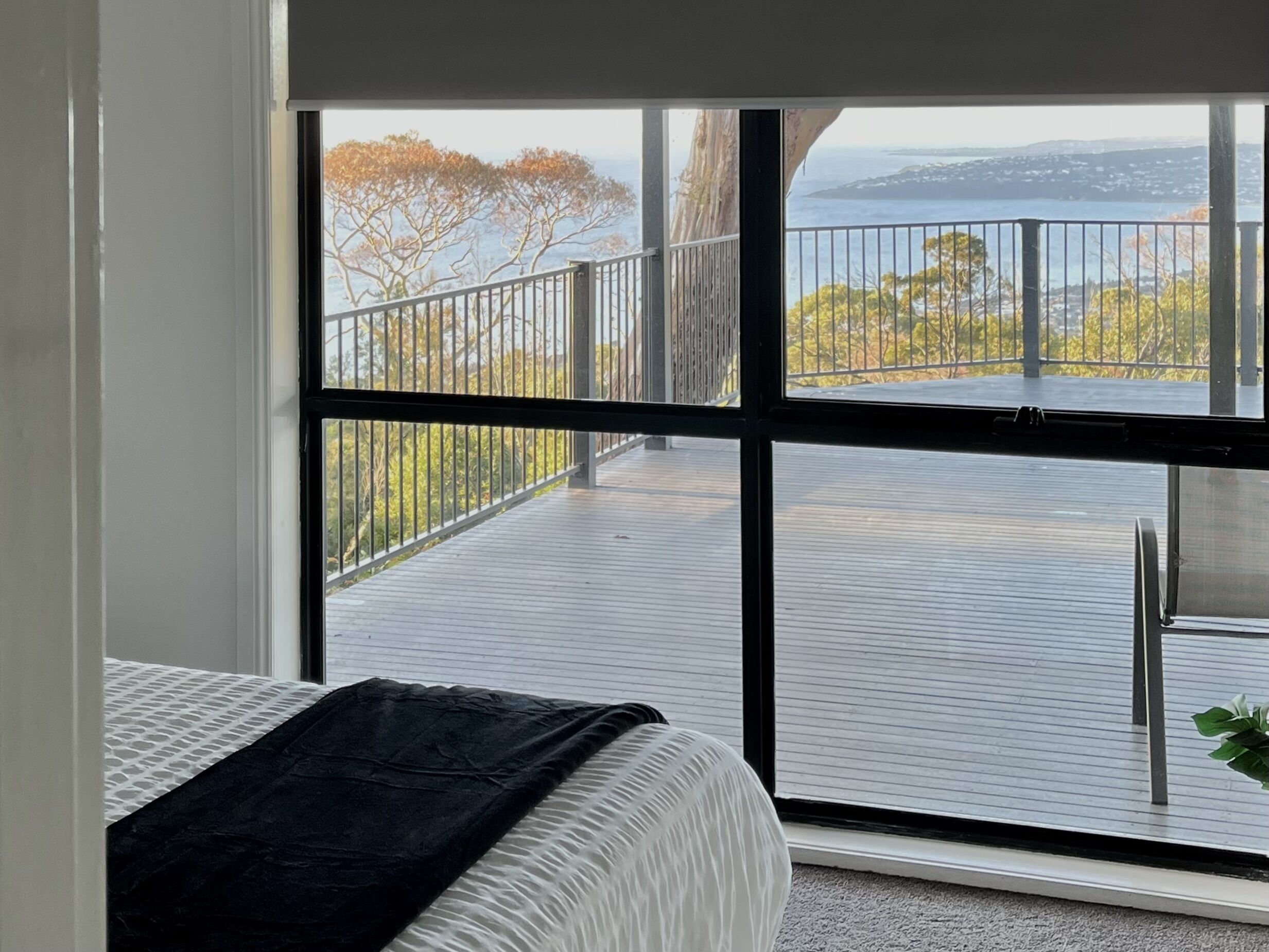 Ein Schlafzimmer mit einem großen Fenster mit Blick auf einen Balkon mit Metallgeländer und Bäumen.