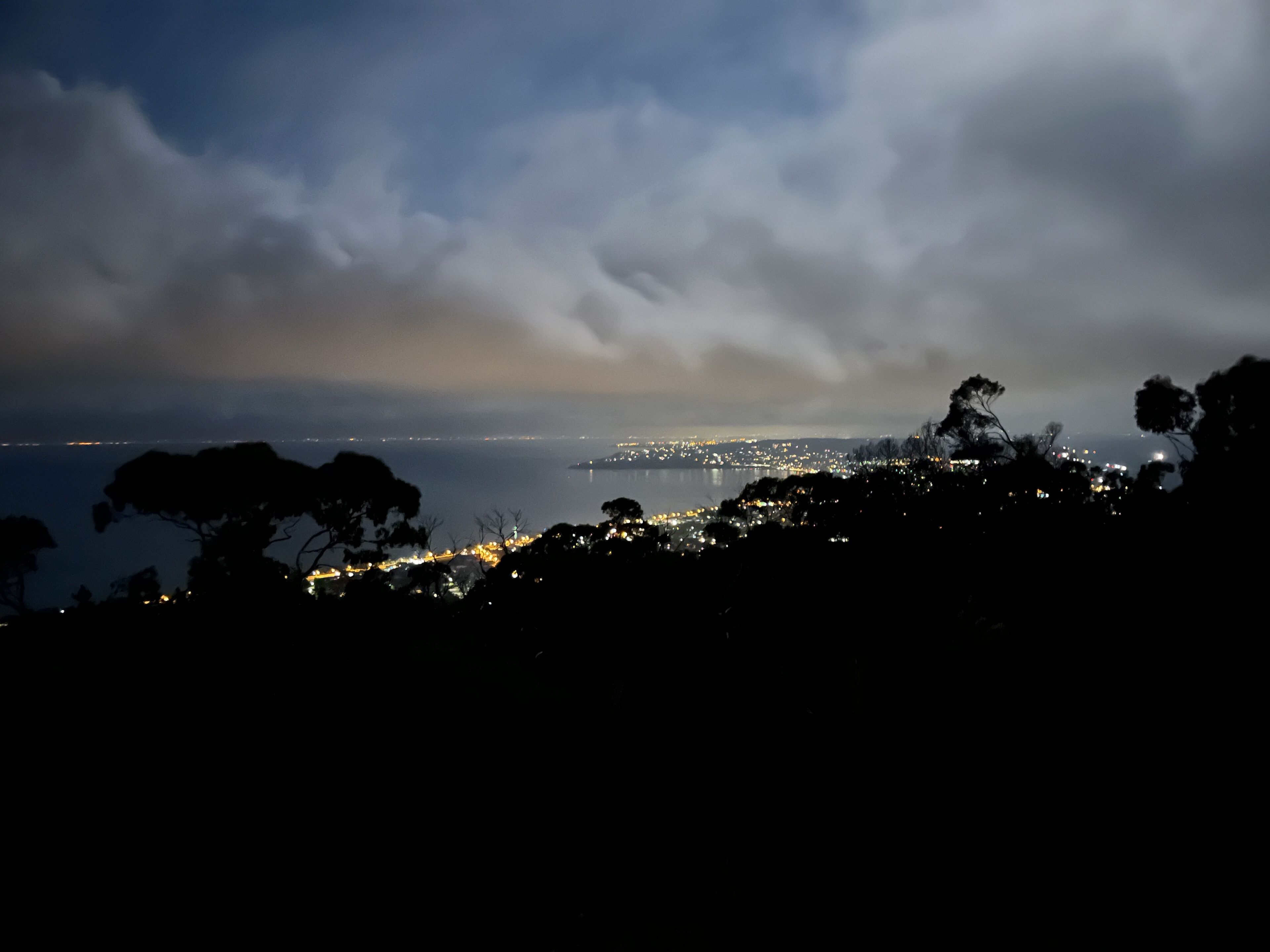 Une vue nocturne d’une ville côtière, avec la mer et les lumières de la ville en arrière-plan.