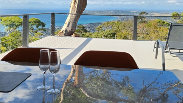 A table with two wine glasses and a view of the ocean and cityscape. - Arthurs Holiday Villa (Arthurs Seat)