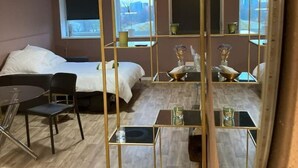 Hotellihuone, jossa on sänky, työpöytä, tuoli, pieni pöytä ja peili, jonka kehys on kullattu.