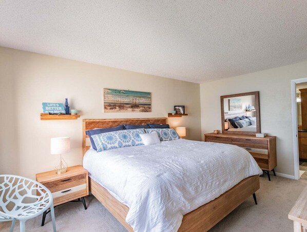 A bedroom with a large bed, bedside tables, a chair, a mirror, and wall decorations.