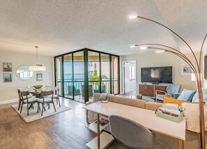 A modern living room with a glass partition, a dining area, and a TV.