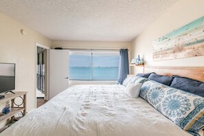 A bedroom with a large bed, a television, and a view of the sea.