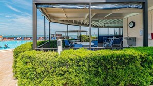 Un espacio de estar al aire libre techado, con sillas y mesas, una piscina y vista al mar.