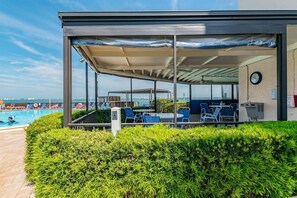Un'area salotto all'aperto coperta con sedie e tavoli, una piscina e vista sul mare.