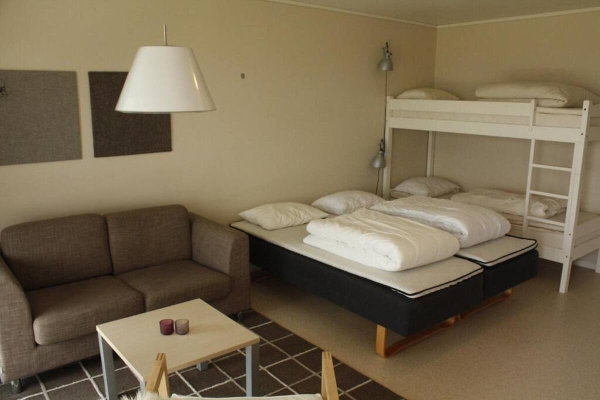A room with a bunk bed, a sofa, a small table, and a lamp.