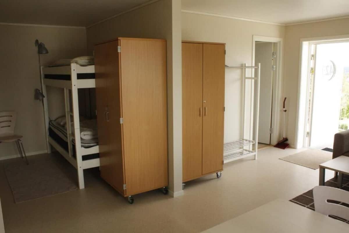 A room with bunk beds, a wooden wardrobe, a desk, and a chair.
