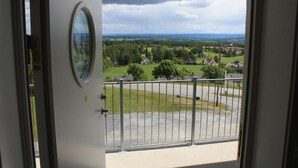 A balcony with a metal railing and a view of a green landscape with houses and trees. - Hedmarktoppen (Hamar)
