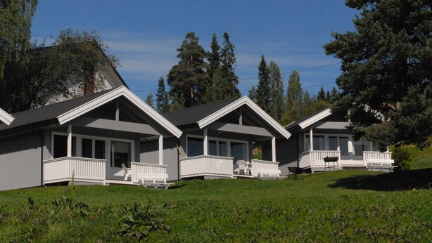 A row of three white cabins with grey roofs, each featuring a porch with white railings and a single chair. - Hedmarktoppen (Hamar)