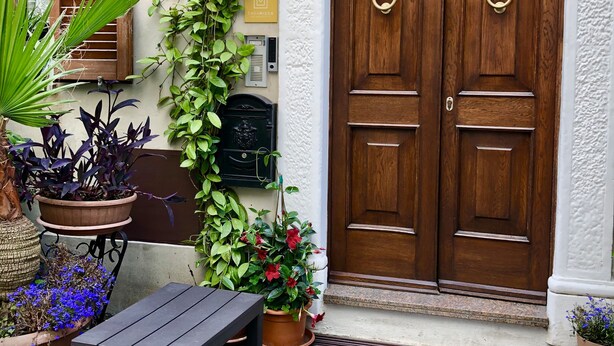 A wooden door with a brass knocker, a potted plant with red flowers, and a small table with a metal stool. - An exclusive terraced house in a very central position, 600 meters from the sea. (San Benedetto del Tronto)
