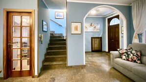 A hallway with a wooden door, a staircase, a couch with floral cushions, and framed artwork on the walls. - An exclusive terraced house in a very central position, 600 meters from the sea. (San Benedetto del Tronto)