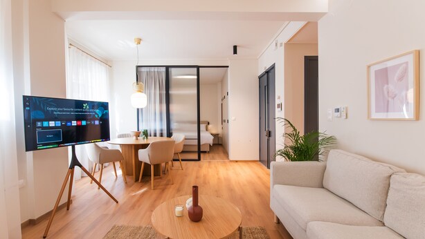 Una sala de estar moderna con un televisor de pantalla plana, una mesa de centro redonda de madera, un sofá color beige y un comedor con mesa y sillas.