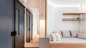Una habitación moderna con una puerta oscura, una pared blanca, suelo de madera, un sofá con cojines y una planta colgante.