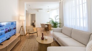 Una sala de estar moderna con una televisión de pantalla plana, un sofá, una mesa de centro y un comedor con sillas y una mesa.