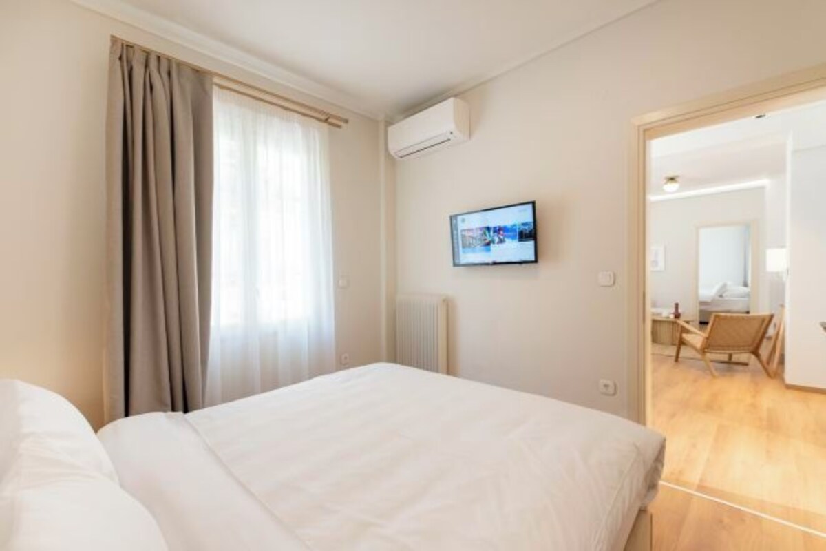 A hotel room with a bed, a television on the wall, and a view into the adjacent room.