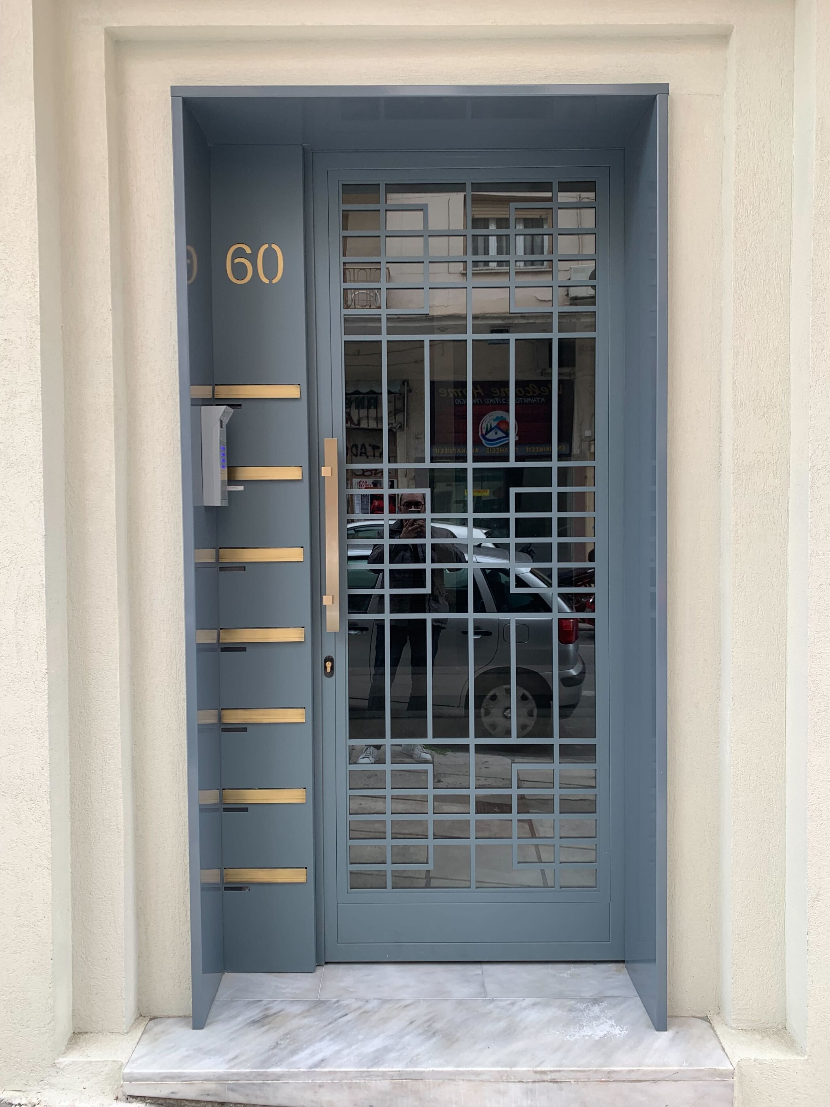 Une porte bleue dotée d’un clavier numérique et d’un portail métallique, donnant accès à un bâtiment dont l’entrée est recouverte de carreaux.