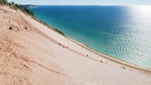 A beach with a clear view of the ocean and a sandy slope. - 🌆One-of-a-Kind Downtown TC Penthouse | Luxe Design + Walk to Bay, Dining, Shops & Events ➠ 400W (Traverse City)