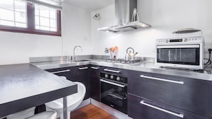 Una cocina moderna con encimera de acero inoxidable, horno empotrado y ventana con persianas.