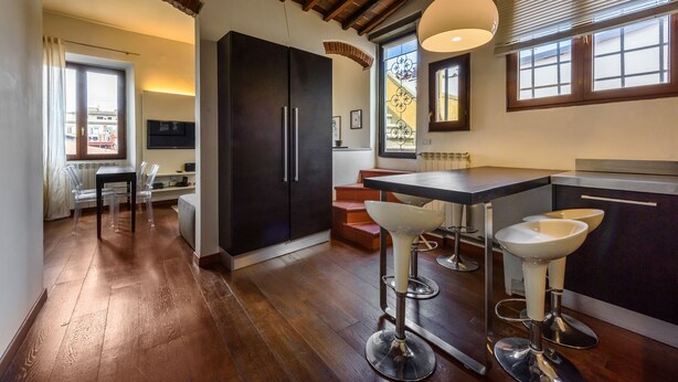 Una cocina moderna con armarios oscuros, una zona de bar con taburetes y una mesa de comedor con sillas.