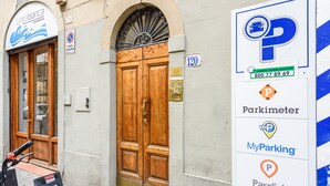 Un edificio con una puerta doble de madera, un cartel con el símbolo 'P' en azul, y un anuncio que enumera servicios de estacionamiento como Parkimeter, MyParking y Google Maps.