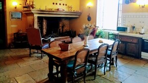 A dining area with a wooden table and chairs, a fireplace, and a kitchen visible through an open door. - CAHORS - Family Manor (Douelle)