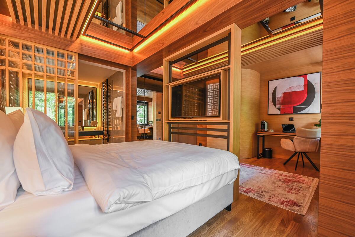A modern bedroom with a large bed, wooden ceiling, and a desk with a chair.