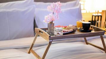 Un plateau de petit-déjeuner sur un lit, avec un vase de fleurs, un verre de jus d’orange et une tasse de café.
