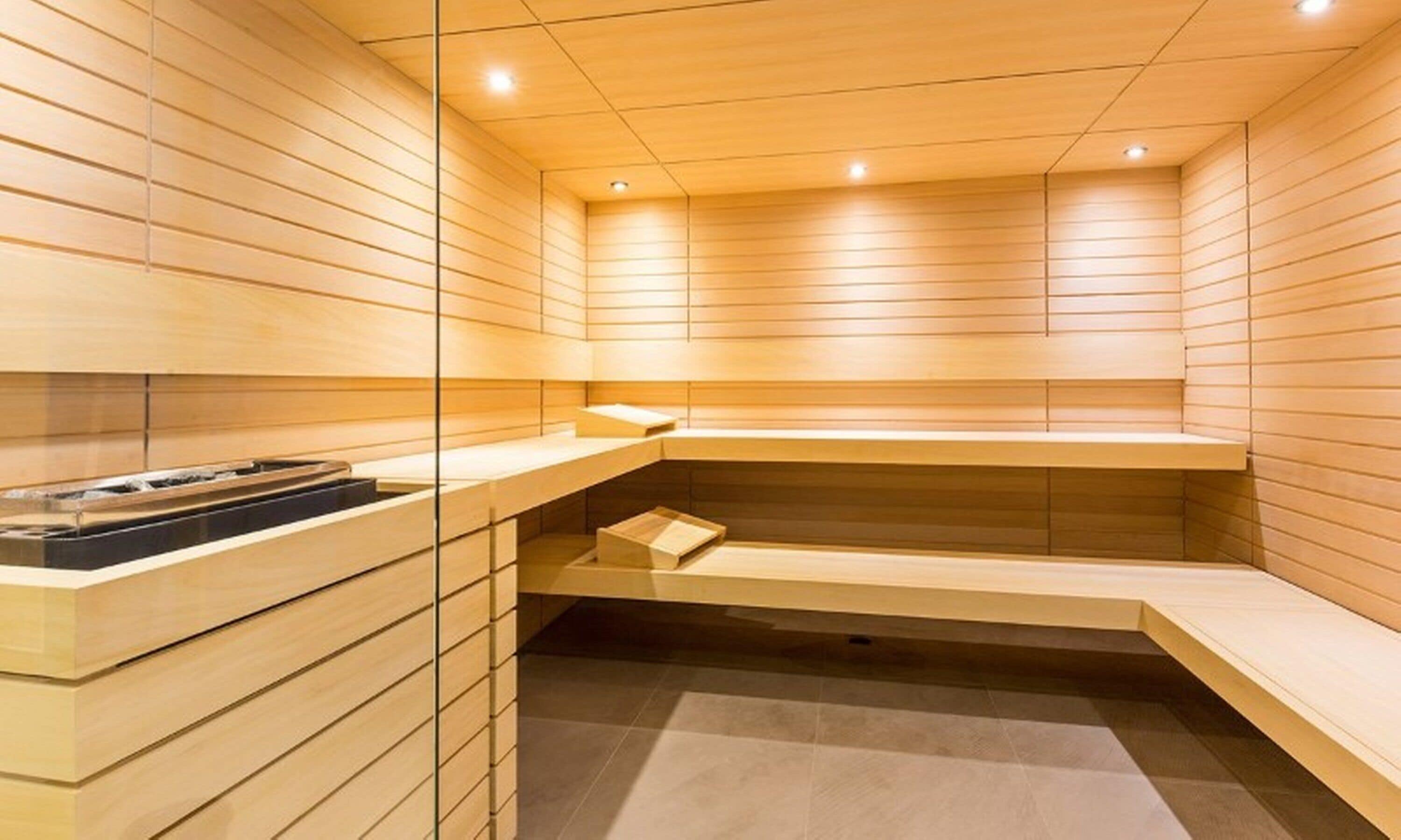 Una sauna con paredes y bancos de madera, un panel de vidrio y un estante con objetos.