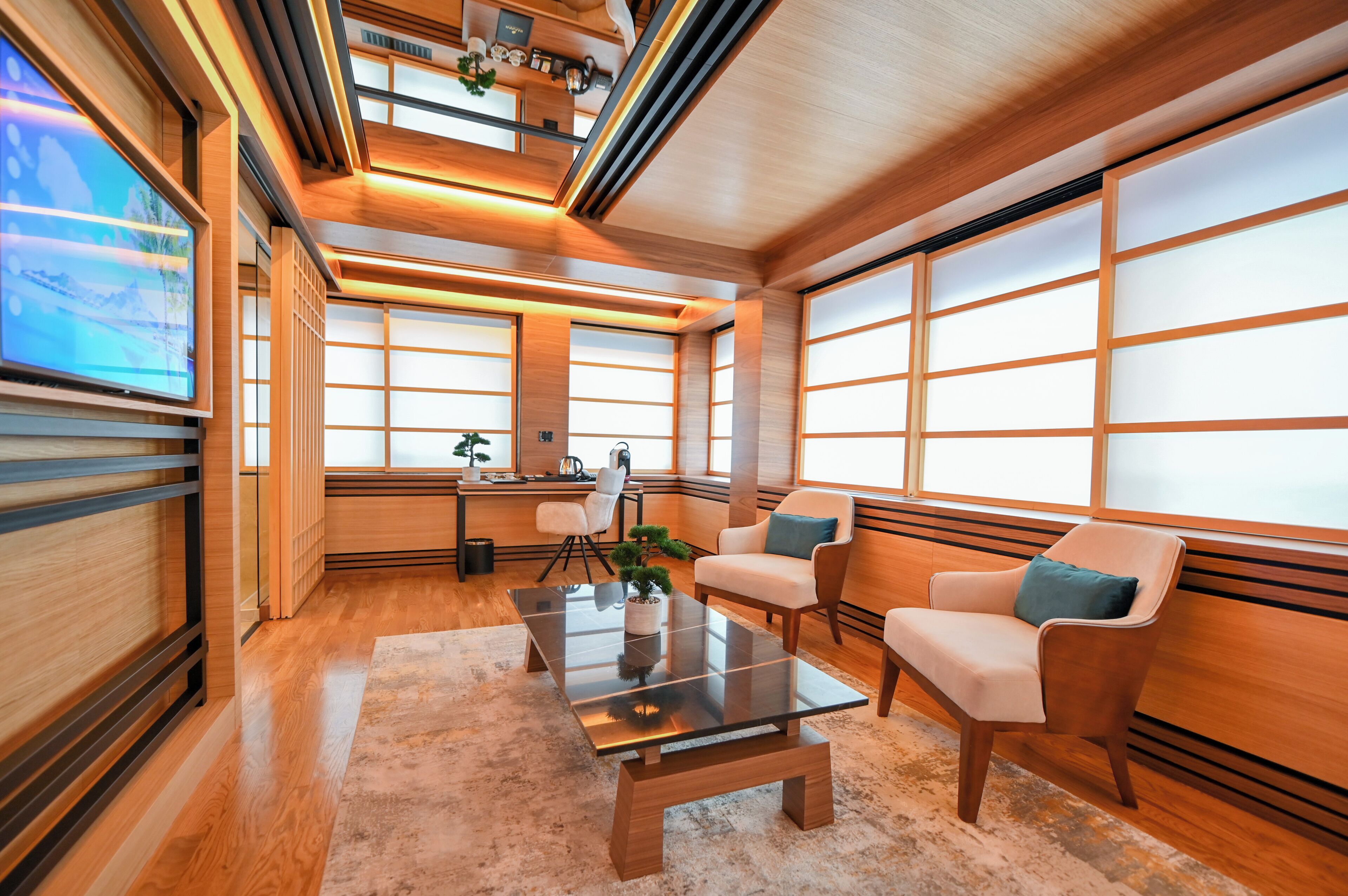 A modern interior with a wooden floor, a glass coffee table, white armchairs, and a television on the left.