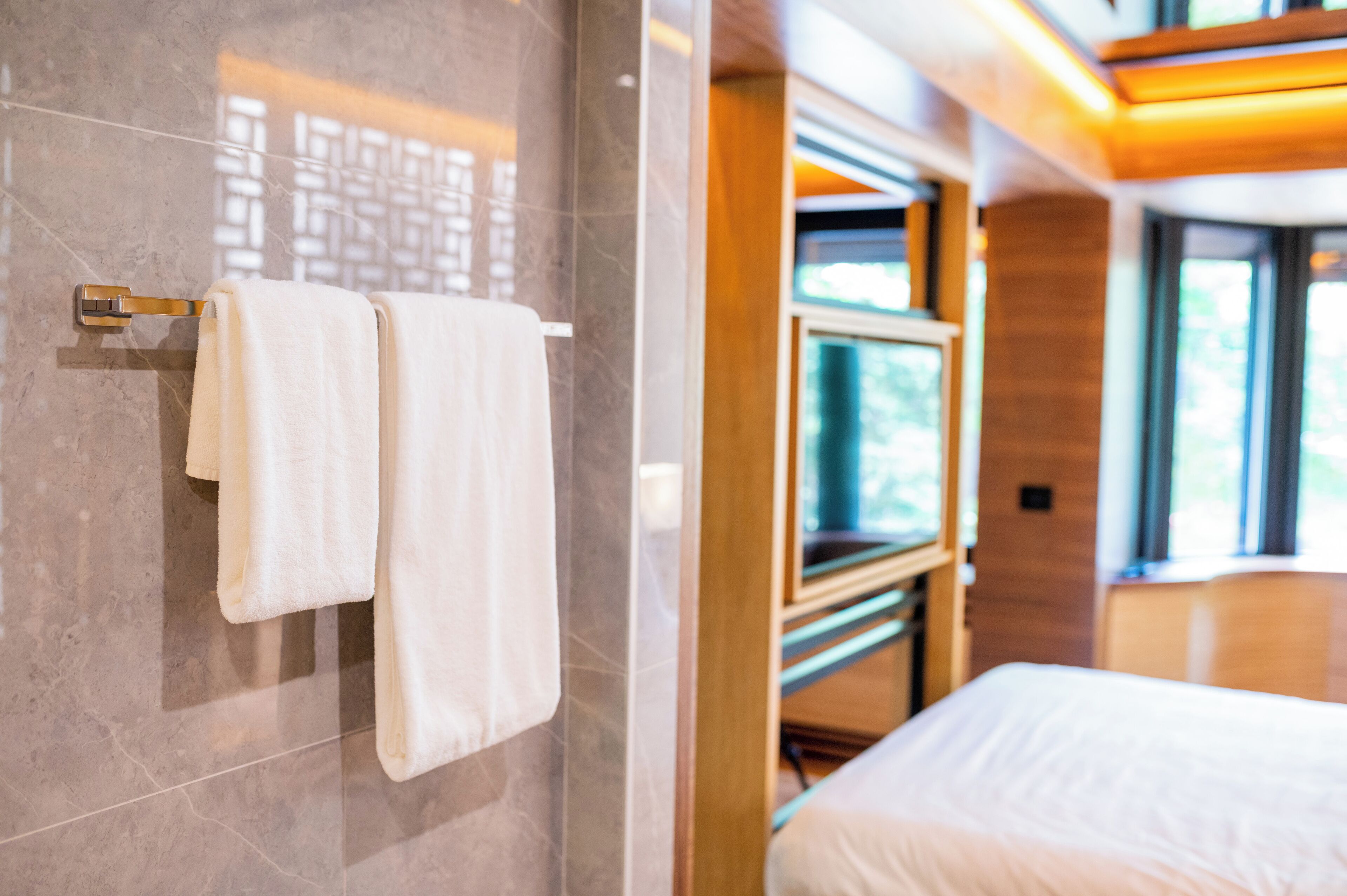 A modern bathroom with a marble wall, a towel rack with two towels, a wooden vanity, and a large mirror.