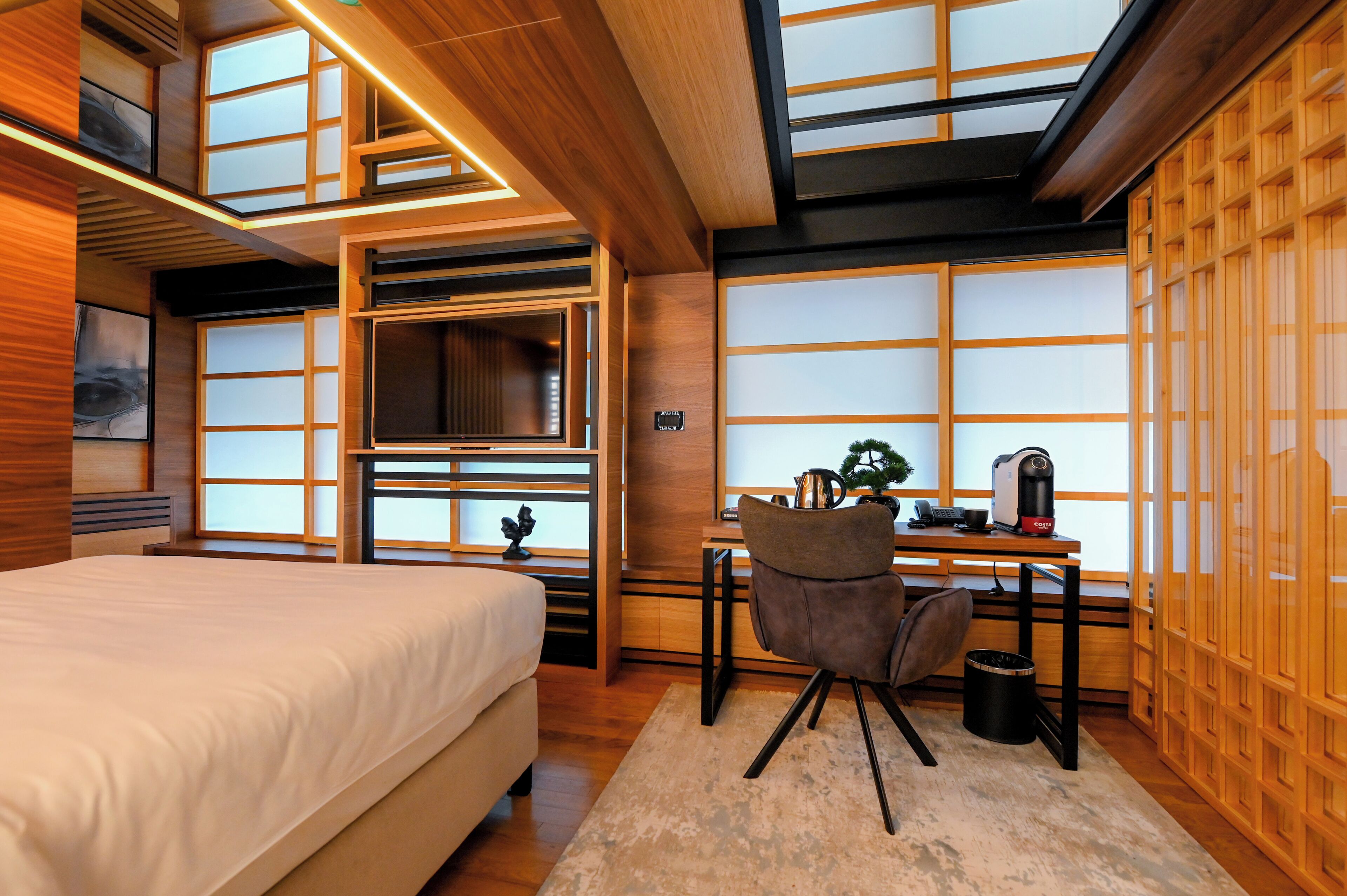A modern bedroom with a large bed, a desk with a chair, and a TV.