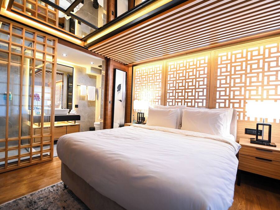 Een moderne hotelkamer met een groot bed, een houten hoofdeinde en een decoratief wandpaneel.