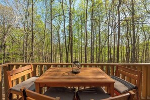 A wooden deck with a table and chairs, surrounded by a forest.