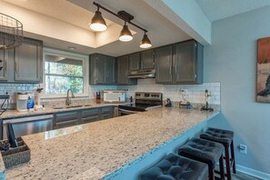 A modern kitchen with granite countertops, dark cabinetry, and a bar stool area.