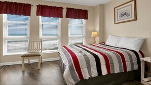 A bedroom with a bed, a chair, two windows with blinds, a lamp, and a framed picture on the wall. - Oceanfront Point Unit with 3 Bedrooms and Great Oceanviews (North Topsail Beach)