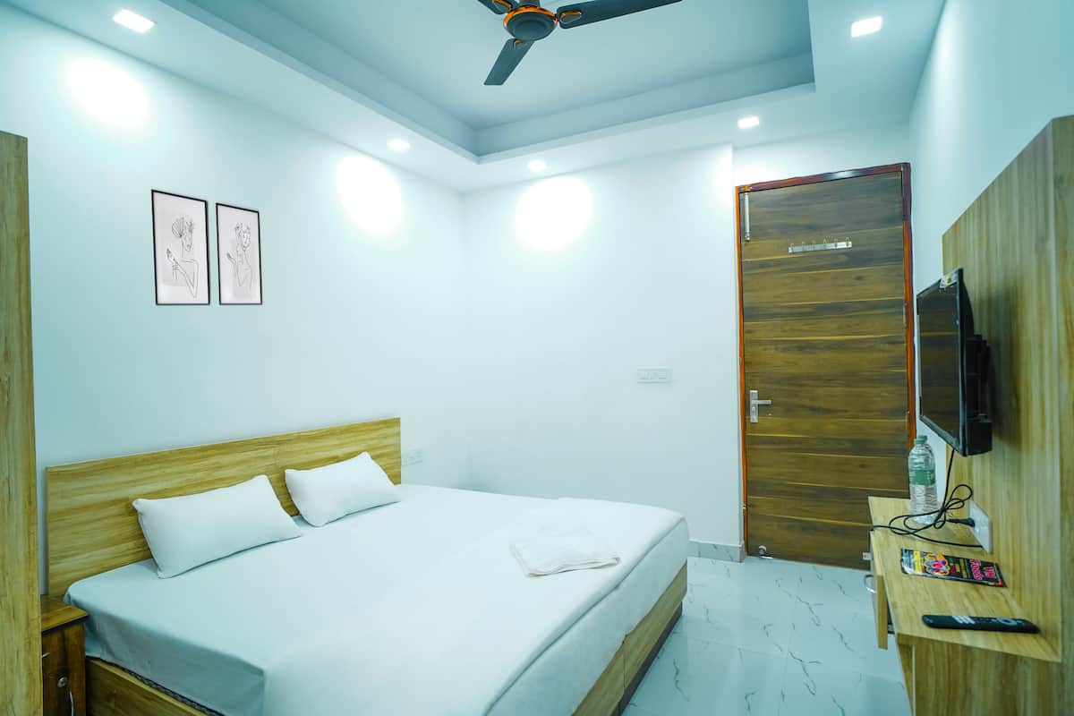 Ein Hotelzimmer mit einem Bett, einem hölzernen Kopfteil, einem Fernseher, einem Schreibtisch mit einer Flasche und einer Fernbedienung sowie zwei gerahmten Bildern an der Wand.
