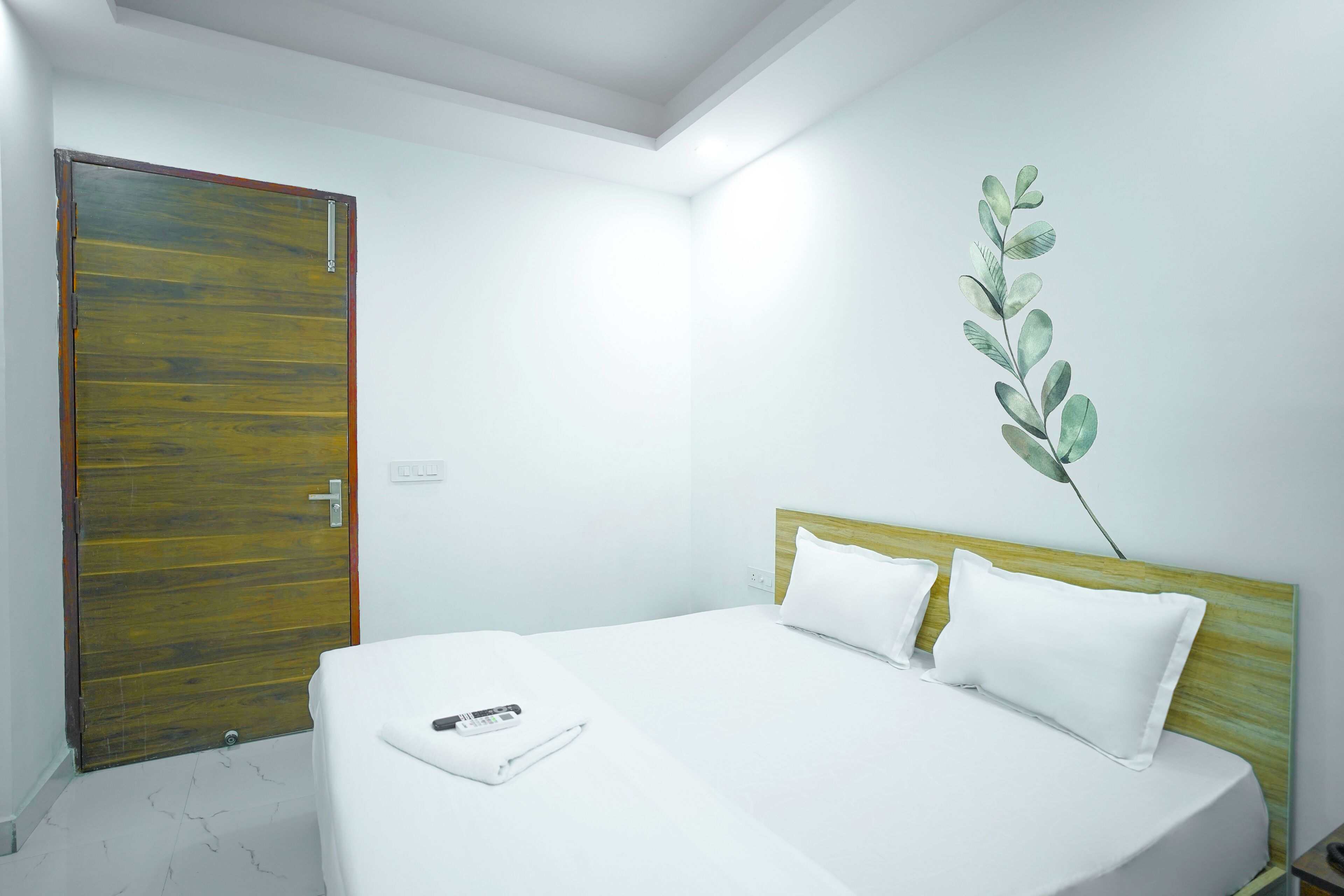 A hotel room with a wooden door, a bed with white bedding, and a wall-mounted plant.