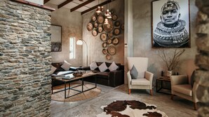A rustic interior with exposed wooden beams, a stone wall, a cowhide rug, and a large framed artwork. - Dream of Africa Bush Lodge (Nkomazi)