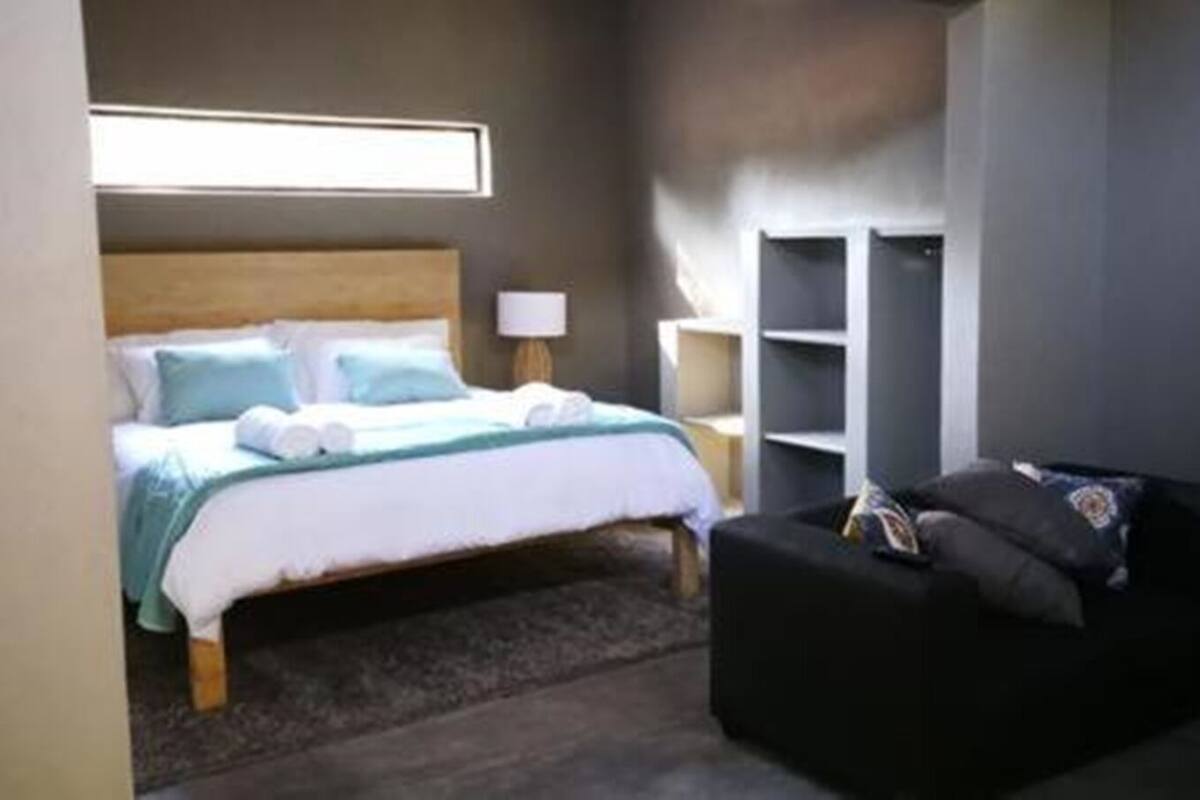 Ein Schlafzimmer mit einem Bett, einem Nachttisch, einer Lampe, einem schwarzen Sofa und integrierten Regalen.