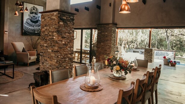 A spacious dining area with a large wooden table, stone pillar, and hanging pendant lights. - Dream of Africa Bush Lodge (Nkomazi)