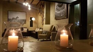 A room with a wooden table, two glass candle holders with lit candles, a sofa, and a wall with a zebra painting. - Dream of Africa Bush Lodge (Nkomazi)