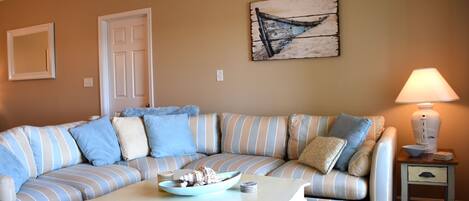 A striped sofa with a bowl of snacks, a small table, a lamp, and a rustic wall art piece.
