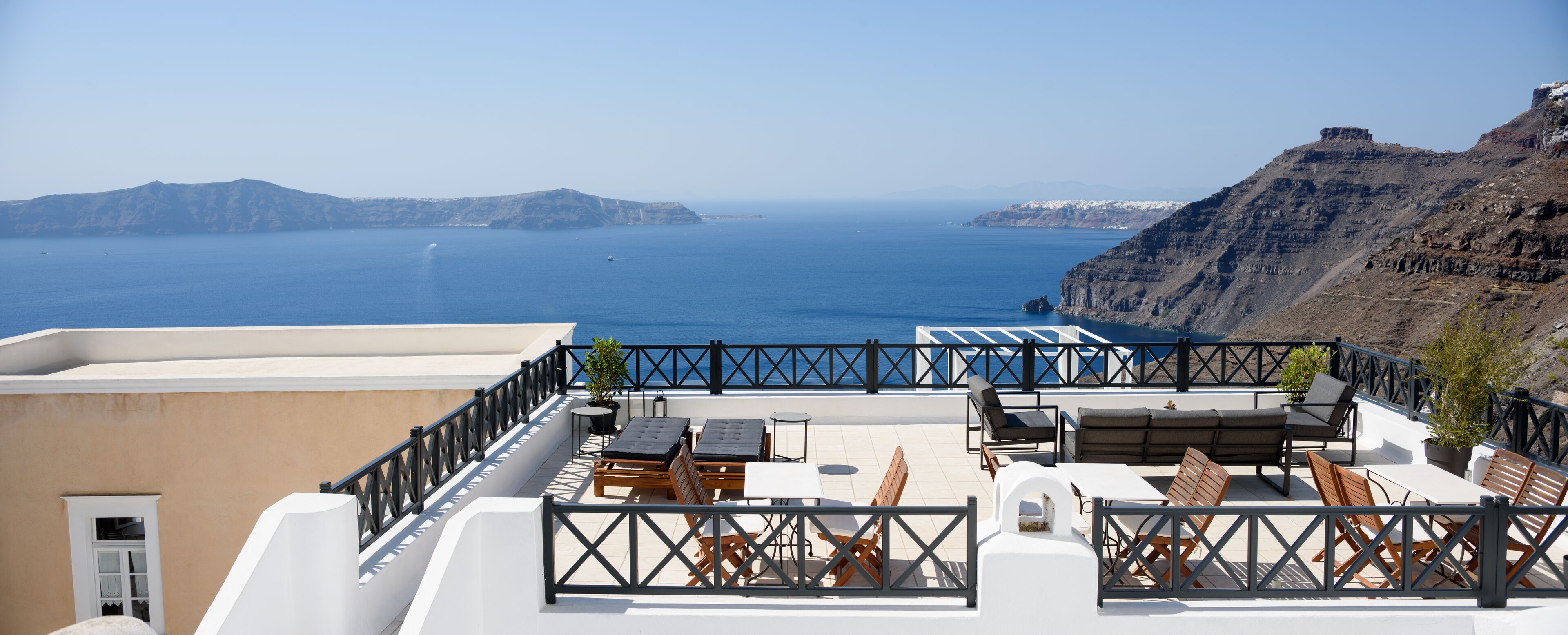 A rooftop terrace with outdoor seating, a view of the sea, and a mountainous landscape.