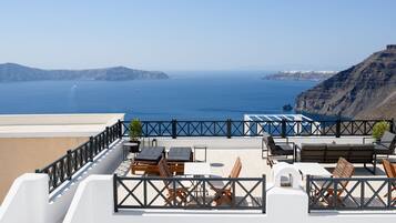 A rooftop terrace with outdoor seating, a view of the sea, and a mountainous landscape.