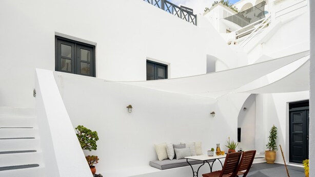 A white building with a staircase, a seating area with cushions, and a table with chairs.