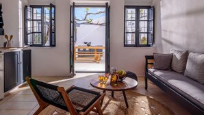 A spacious living area with a high ceiling, a sofa, a coffee table with drinks, and a view of the outdoors through large windows. - Firalia Suites (Santorini)