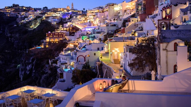 A coastal town with white buildings, a prominent church, and a view of the sea. - Firalia Suites (Santorini)