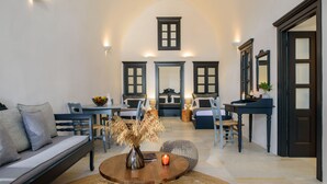 A spacious living area with a high arched ceiling, a round wooden coffee table, a sofa, and a dining table with chairs. - Firalia Suites (Santorini)